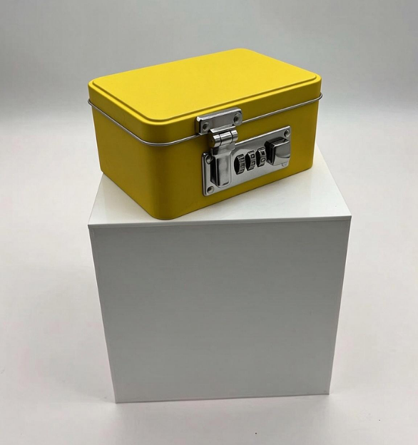 Front and three-quarter views of the supplied yellow rectangular tin box with an external latch and three-digit combination lock. Dimensions and specifications must be confirmed from production drawings.